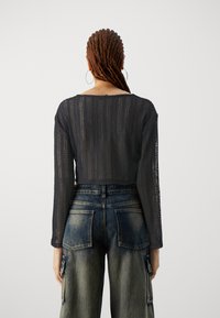 Knitted navy cropped sweater with long sleeves and open weave detail, paired with high-waisted faded blue jeans featuring large pockets.