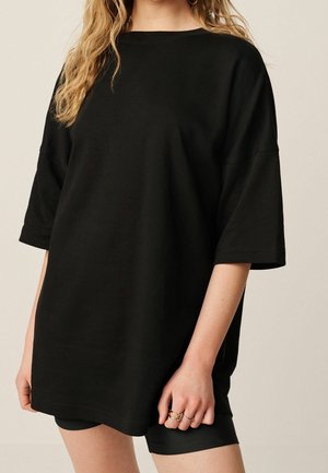 T-shirt noire surdimensionnée en coton doux avec des manches courtes, un col rond et une coupe décontractée, associée à un short noir.