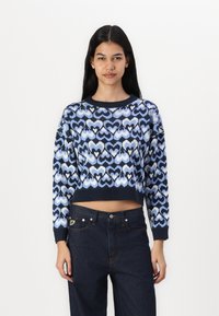 Blue cropped sweater featuring a heart pattern in varying shades with a ribbed neckline and cuffs, paired with dark blue jeans.