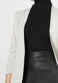 Jasnoszara marynarka na czarnym prążkowanym golfie, w połączeniu z czarną skórzaną spódnicą. Marynarka ma gładką fakturę i minimalistyczny design.