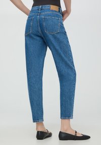 Jasnoniebieskie spodnie z wysokim stanem o prostym kroju, tekstura dżinsu, dwie tylne kieszenie oraz brązowa skórzana łatka na pasku.