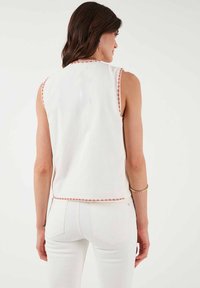 Witte mouwloze top met decoratieve rode en roze stiksels langs de halslijn en zoom, met een relaxte pasvorm en zachte textuur.