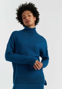 Maglione blu a collo alto con polsini e orlo a costine, caratterizzato da una vestibilità rilassata e spacchi laterali. Il tessuto morbido e testurizzato aggiunge comfort.