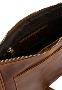 Vnitrní prostor hnědé kožené tašky se zipovou kapsou, hladkou texturou a označením z kůže. Obsahuje kovový zip s kontrastní textilní podšívkou.