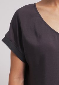 Mørkegrå v-hals top med korte, rullede ærmer. Stoffet ser glat og let ud, og har en afslappet pasform.