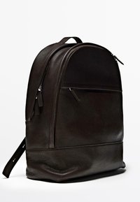 Brown leather backpack with a rounded shape, a front zip pocket, and shoulder straps. Smooth texture with subtle stitching details.