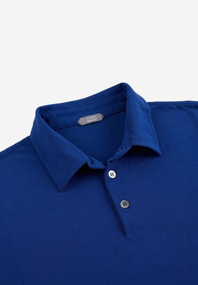 Polo de color azul marino hecho de algodón, con un cuello clásico, tapeta de tres botones y textura suave. Etiqueta visible dentro del cuello.