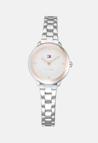 Silver metal linked wristwatch with round white face, gold-tone hour markers and hands, and a small red, white, and blue logo at 12 o'clock.