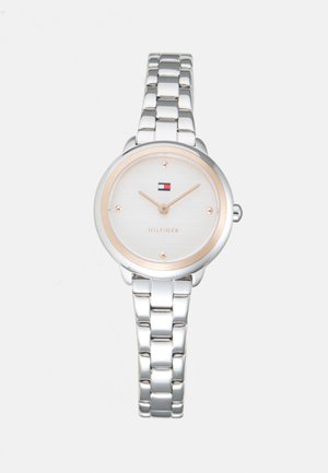 Silbernes Metallarmbanduhr mit rundem weißen Ziffernblatt, goldfarbigen Stundenmarkierungen und -zeigern sowie einem kleinen rot-weißen und blauen Logo auf der 12-Uhr-Position.