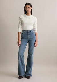 Hoge taille, lichtblauwe flared jeans met een gladde denimtextuur. Gepaard met een aansluitend, geribbeld wit longsleeve shirt.