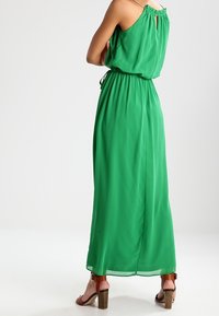 Grön, ärmlös maxiklänning med cinchad midja, flödande tyg och en nyckelhål baktill. Matchad med bruna klacksandaler.