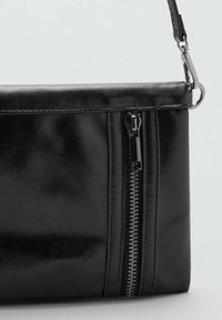 Svart läderhandväska med en slät textur, som har en framträdande dragkedjedetalj på sidan och en smal, justerbar rem.