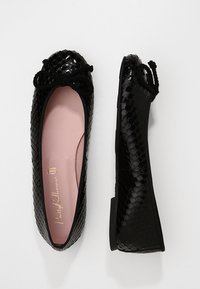 Svarta lackskinnsballetskor med ett vävt mönster, rund tå och en rosett på framsidan. Ljusrosa foder inuti.