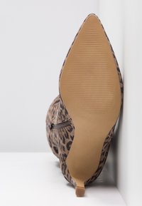 Chaussure à talon haut en imprimé léopard avec un bout pointu, tissu texturé et un detail zippé sur le côté. Semelle plate et texturée.