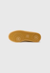 Suola di scarpa in gomma color sabbia con un motivo a zig zag e due accenti circolari. Superficie texturizzata per una maggiore aderenza. Forma piatta e arrotondata.