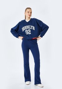 Granatowy sweter z nadrukiem "BROOKLYN 92", w luźnym fasonie. W zestawie z pasującymi granatowymi spodniami sportowymi z białymi bocznymi paskami.