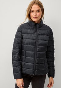 Zwarte pufferjack met een hoge kraag, doorgestikte design en een ritssluiting aan de voorkant. Het materiaal lijkt glanzend en glad, biedt isolatie en warmte.