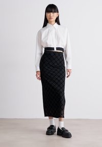Chemise blanche à boutons avec un design court, associée à une jupe noire texturée arborant un motif en losange, et des chaussures noires chunky.