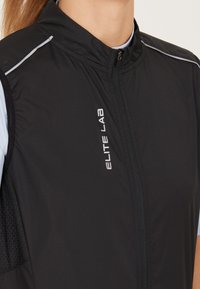 Schwarze Weste mit hohem Kragen, leichtem Stoff, reflektierenden Akzenten und einem Reißverschluss, mit "ELITE LAB" Branding auf der Vorderseite.