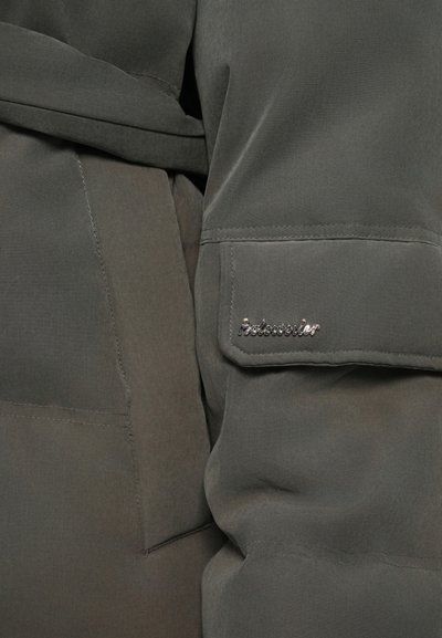 Close-up van een donkergrijze jasstof met een klein metallic "Holoworker" logo op een rechthoekige zakflap.
