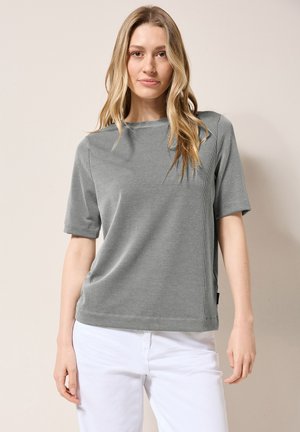 Grijze geribbelde t-shirt met korte mouwen, losse pasvorm en een ronde hals. Gecombineerd met witte broek, die een zachte textuur en subtiele glans toont.