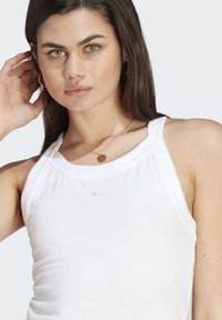 Débardeur de sport blanc avec un col rond. Présente un logo discret en bleu clair sur la poitrine. Texture lisse et design ajusté.