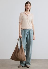 Ροζ ανοιχτό ροζ κοντομάνικο πόλο, με άνετη εφαρμογή, σε συνδυασμό με φαρδιά ξεβαμμένα μπλε τζιν. Καφέ τσάντα με υφή και ιμάντα ώμου. Μπεζ παπούτσια.