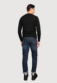 Suéter negro con cuello redondo, combinado con jeans azul oscuro que tienen bajos acampanados. El atuendo incluye zapatos negros informales.