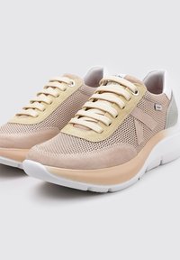 Zapatillas deportivas beige con materiales de malla y ante; presentan cordones crema, un tacón blanco y una suela acolchada de color claro.