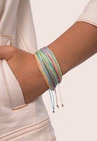 Braccialetti elastici multicolori con tonalità pastello, caratterizzati da design con cordoncini sottili e piccoli dettagli metallici, indossati su un polso.