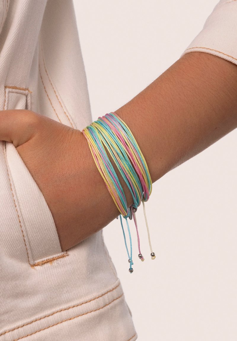 Braccialetti elastici multicolori con tonalità pastello, caratterizzati da design con cordoncini sottili e piccoli dettagli metallici, indossati su un polso.