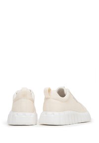 Zapatillas de lona beige con una suela de goma blanca texturizada. Cuenta con un cuello acolchado y una asa para ponerlas fácilmente. Diseño minimalista.