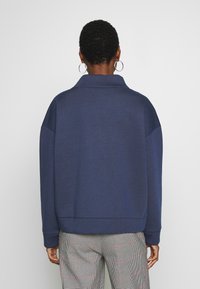 Felpa oversize blu navy con colletto alto, bordo a costine e maniche ampie. Il tessuto appare liscio, con una vestibilità casual e rilassata.