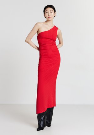 Rotes, einseitiges Kleid mit taillierter Silhouette, strukturiertem Stoff und Raffungen. Getragen mit schwarzen kniehohen Stiefeln.