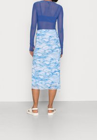 Pitkä sininen hame, jossa on aalto-osa kuvioita, valmistettu kevyestä kankaasta. Yhdistetty läpinäkyvän pitkähihainen paidan kanssa. Valkoiset sandaalit täydentävät asun.