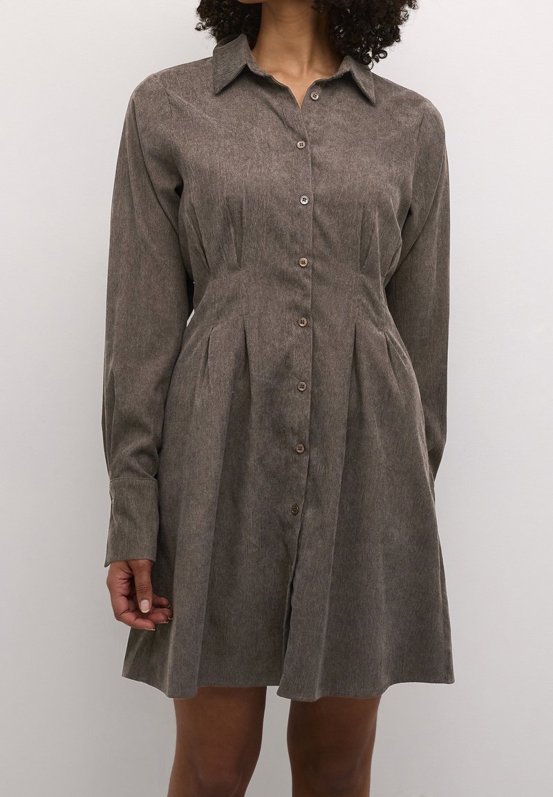 Robe-chemise en velours côtelé marron à manches longues, fermeture par boutons et design plissé, avec col et texture douce.