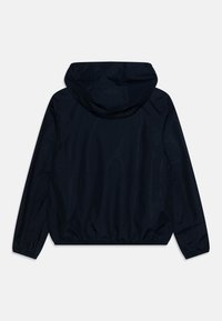 Veste à capuche navy fabriquée en tissu lisse et léger. Elle présente des poignets et un ourlet élastiques pour un ajustement parfait. Design minimaliste sans matériel visible.