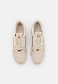 Paio di sneakers beige con suole bianche, dettagli dorati, pannelli laterali in rete e lacci, viste dall'alto su uno sfondo bianco.