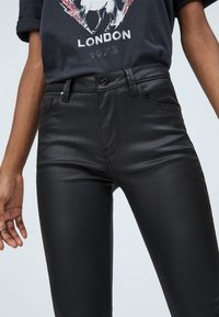 Czarne spodnie slim-fit wykonane z miękkiego materiału, z rozporkiem na zamek, przednimi kieszeniami oraz subtelnymi detalami przeszycia wzdłuż boków i pasa.