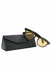 Occhiali da sole neri con lenti gialle, caratterizzati da una forma a occhio di gatto e un design elegante, appoggiati accanto a un astuccio triangolare nero texturizzato.