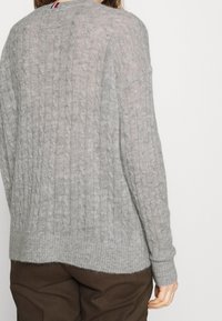 Pull gris à maille torsadée avec un col arrondi, des manches longues et un ourlet légèrement asymétrique. Texture douce avec des poignets côtelés.