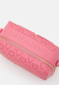 Rosa Valentino-väska i strukturerat läder, präglad logotyp och guldzipper. Har en elegant form och ett subtilt mönster av upprepad varumärkeslogotyp.