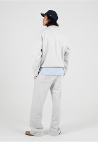 Grijze sweatshirt met een relaxte pasvorm, gelaagd over een lichtblauw gestreept shirt. Gecombineerd met bijpassende grijze broek en een marineblauwe baseballpet.