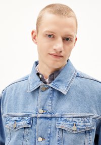 Lichtblauwe denimjas met een spitse kraag, zilveren knopen en borstzakken. Glad materiaal met een lichte vervaging op de stof.