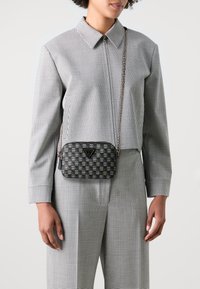 Geantă crossbody în carouri negre și gri, cu închidere cu fermoar, accesorii aurii și curea din lanț. Are un detaliu cu logo pe partea din față.