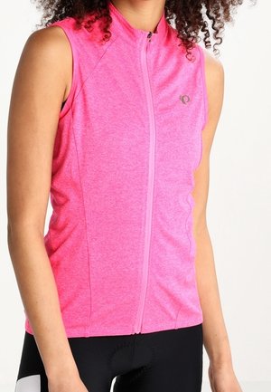 Mujer vistiendo un chaleco de ciclismo sin mangas y de color rosa brillante con cremallera, y pantalones cortos de ciclismo negros, mostrada desde los hombros hasta las caderas.