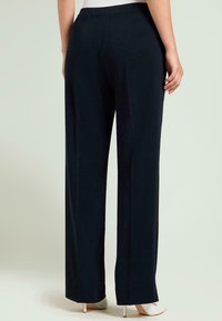 Marineblauwe wijde broek met een gladde textuur en strakke lijnen. Voorzien van een getailleerde tailleband en een comfortabele pasvorm, gecombineerd met witte schoenen met hak.