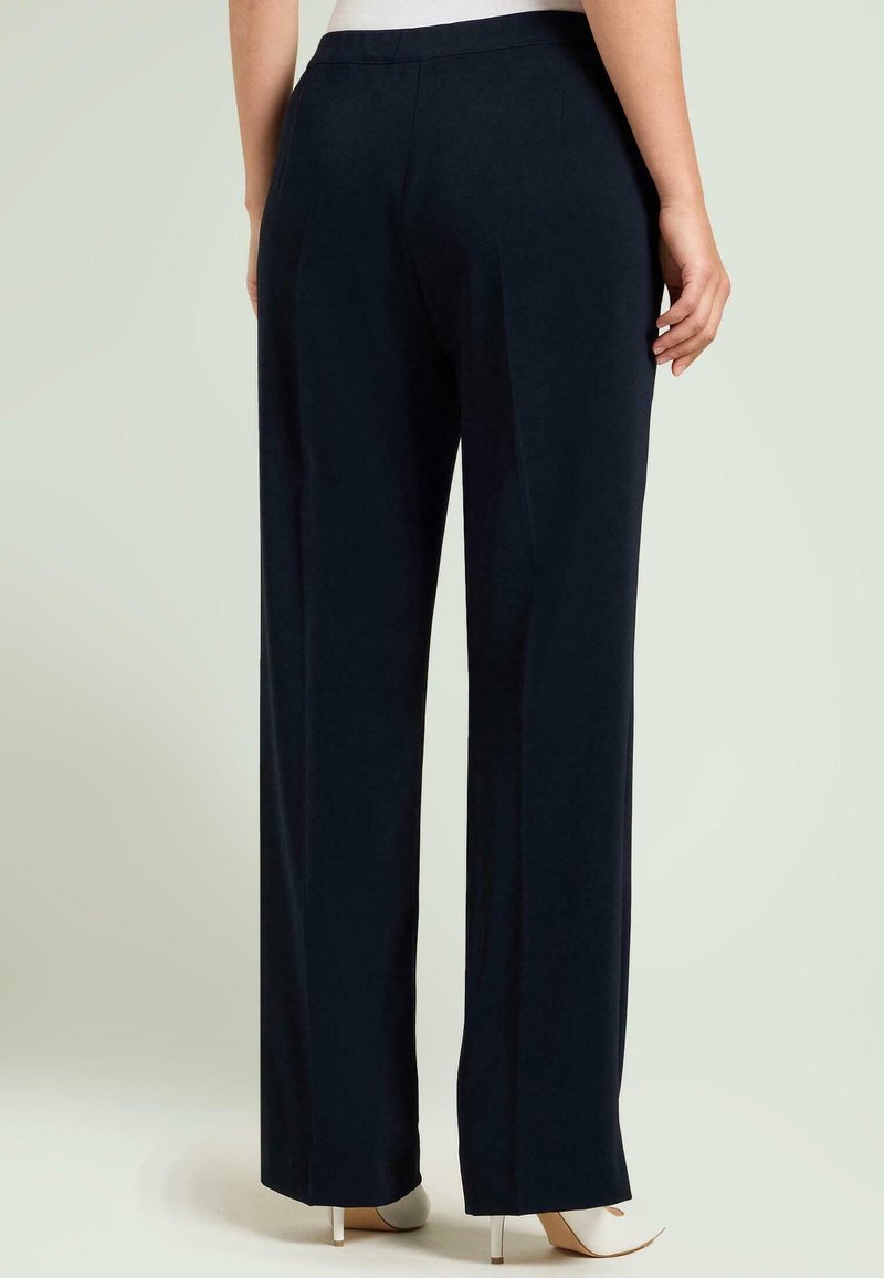 Marineblauwe wijde broek met een gladde textuur en strakke lijnen. Voorzien van een getailleerde tailleband en een comfortabele pasvorm, gecombineerd met witte schoenen met hak.