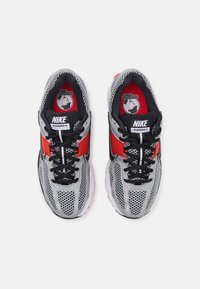 Tenisky Nike Vomero 5 s šedým síťovaným svrškem, červenými detaily, černými tkaničkami, polstrovanou podrážkou a značkovými vložkami.