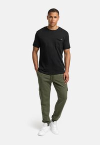 Black cotton t-shirt with a chest pocket, paired with olive green cargo pants, featuring side pockets, completed with white sneakers.